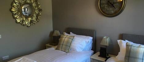 Habitación de hotel con dos camas, un reloj de pared redondo, un espejo decorativo y una lámpara de pared.