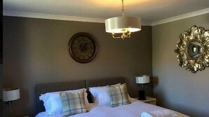 A neatly made bed with pillows and a folded towel, a bedside lamp, a wall clock, and a decorative mirror.