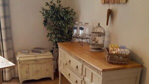 A room with a wooden dresser, a small table with a plant, a basket of books, and a wall-mounted birdcage.