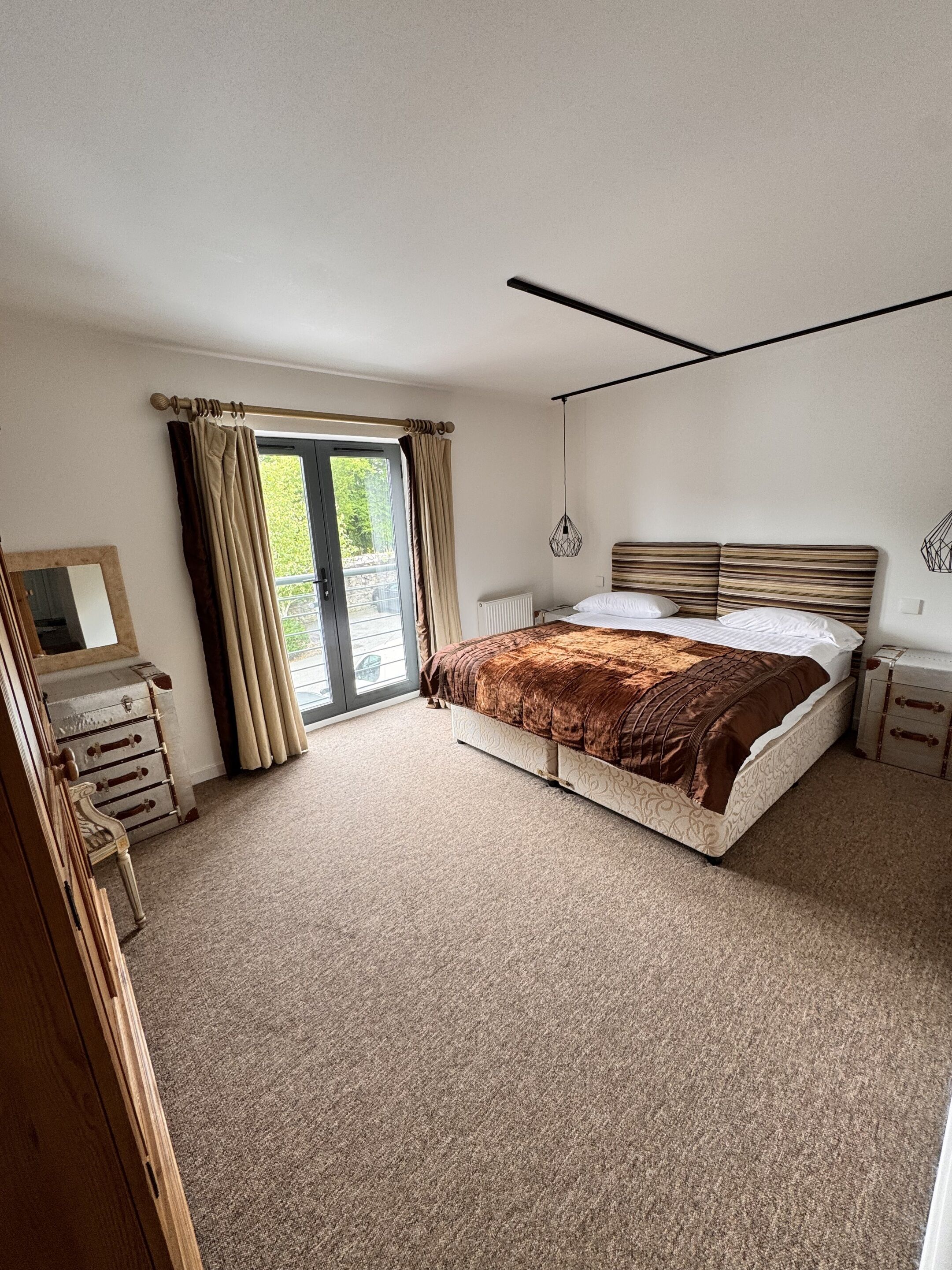 A bedroom with a large bed, a dresser, a mirror, and a window with curtains.