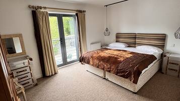 A bedroom with a large bed, a dresser, a mirror, and a window with curtains.