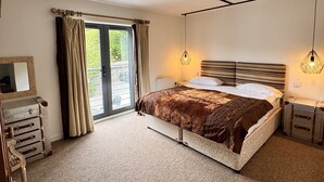 Ein Schlafzimmer mit einem großen Bett, einem Schminktisch, einem Nachttisch, einem Spiegel und einer Schiebetür zum Außenbereich.