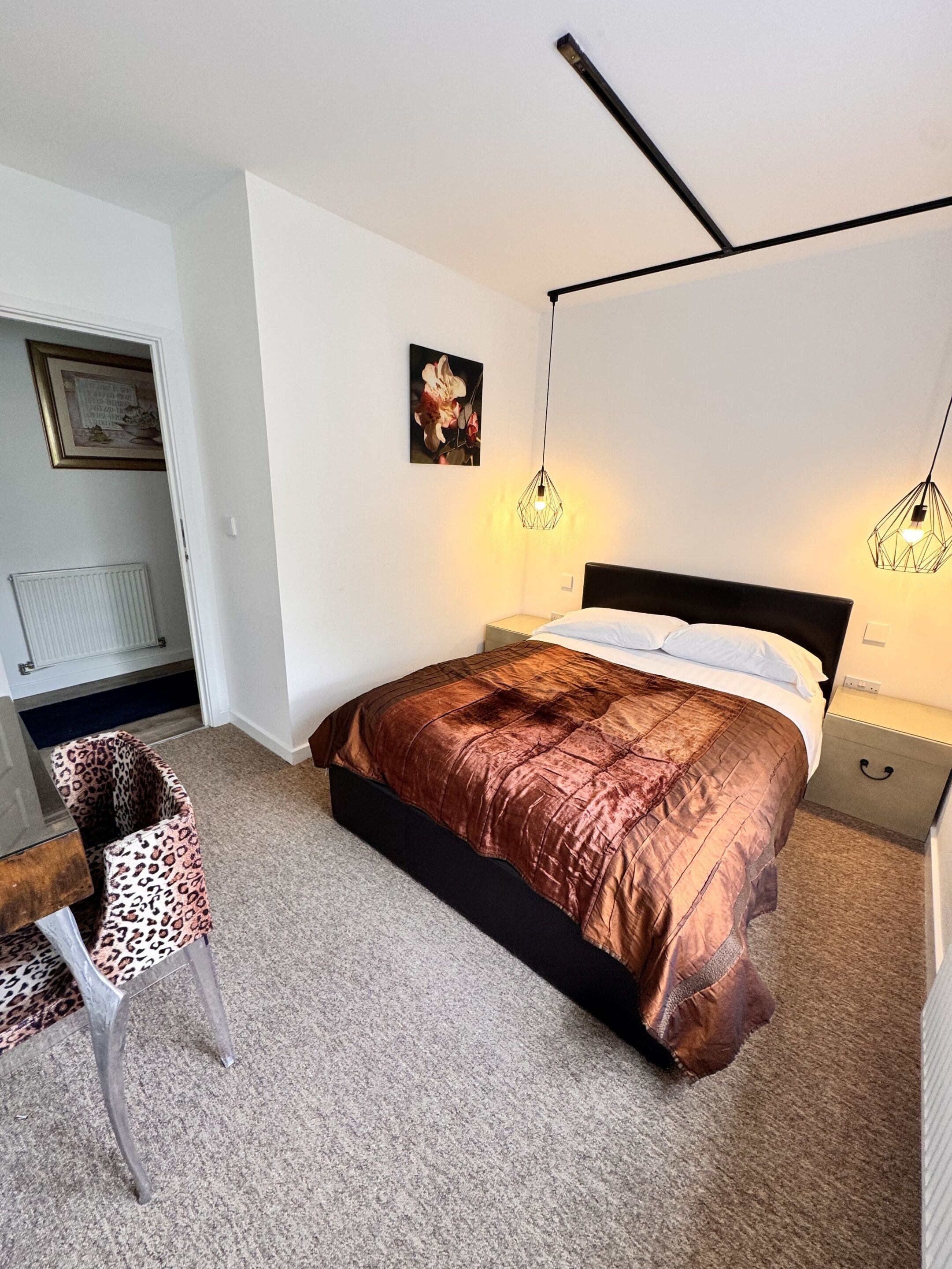 A bedroom with a bed, a chair, a bedside table, and a hanging light fixture.