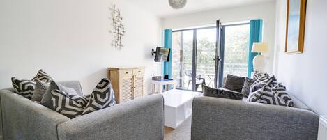 A living room with two grey sofas, a wooden cabinet, a TV, and a balcony with blue curtains.