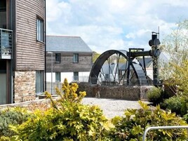 A building with a large water wheel, stone walls, and a courtyard with plants.