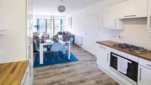Eine moderne Küche mit weißen Schränken, einem Gasherd und einem Essbereich mit blauen Stühlen und einem blauen Teppich.