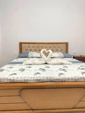 Een bed met een bloemenbedekking, een handdoekarrangement in de vorm van een hart, en een houten hoofdbord.