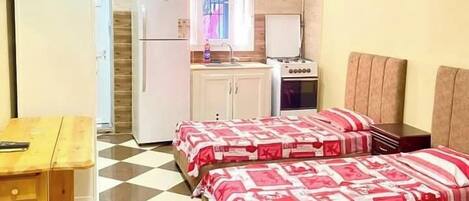 Une chambre avec deux lits, une petite cuisine, une table à manger et un sol à carreaux.