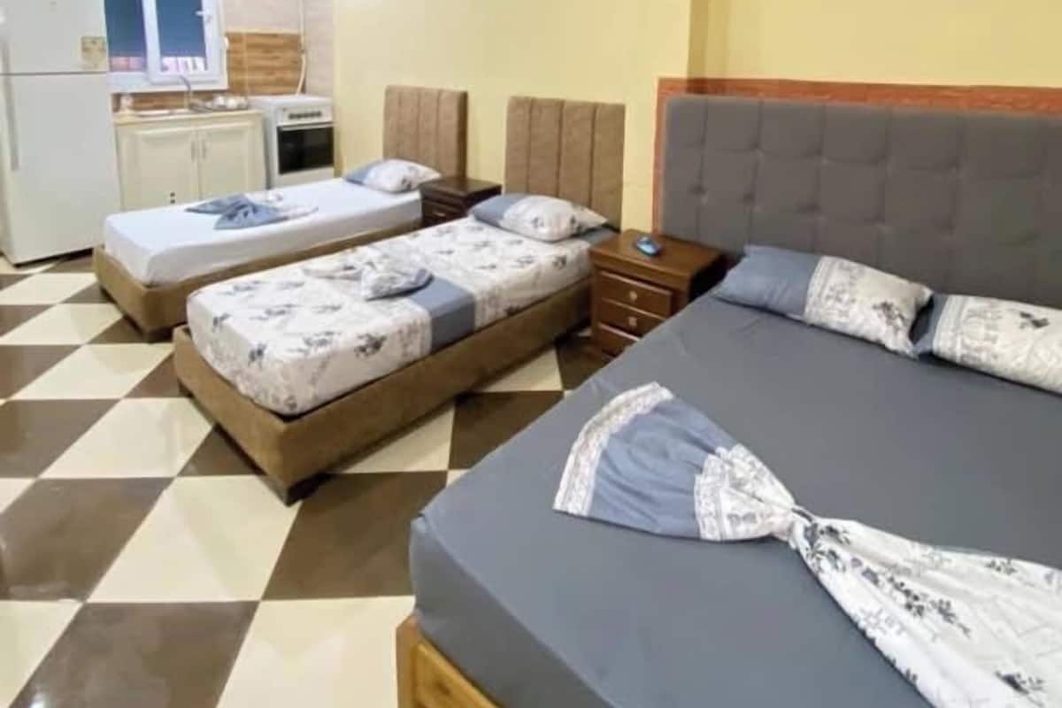 A hotel room with two beds, a small kitchenette, and a checkered floor.