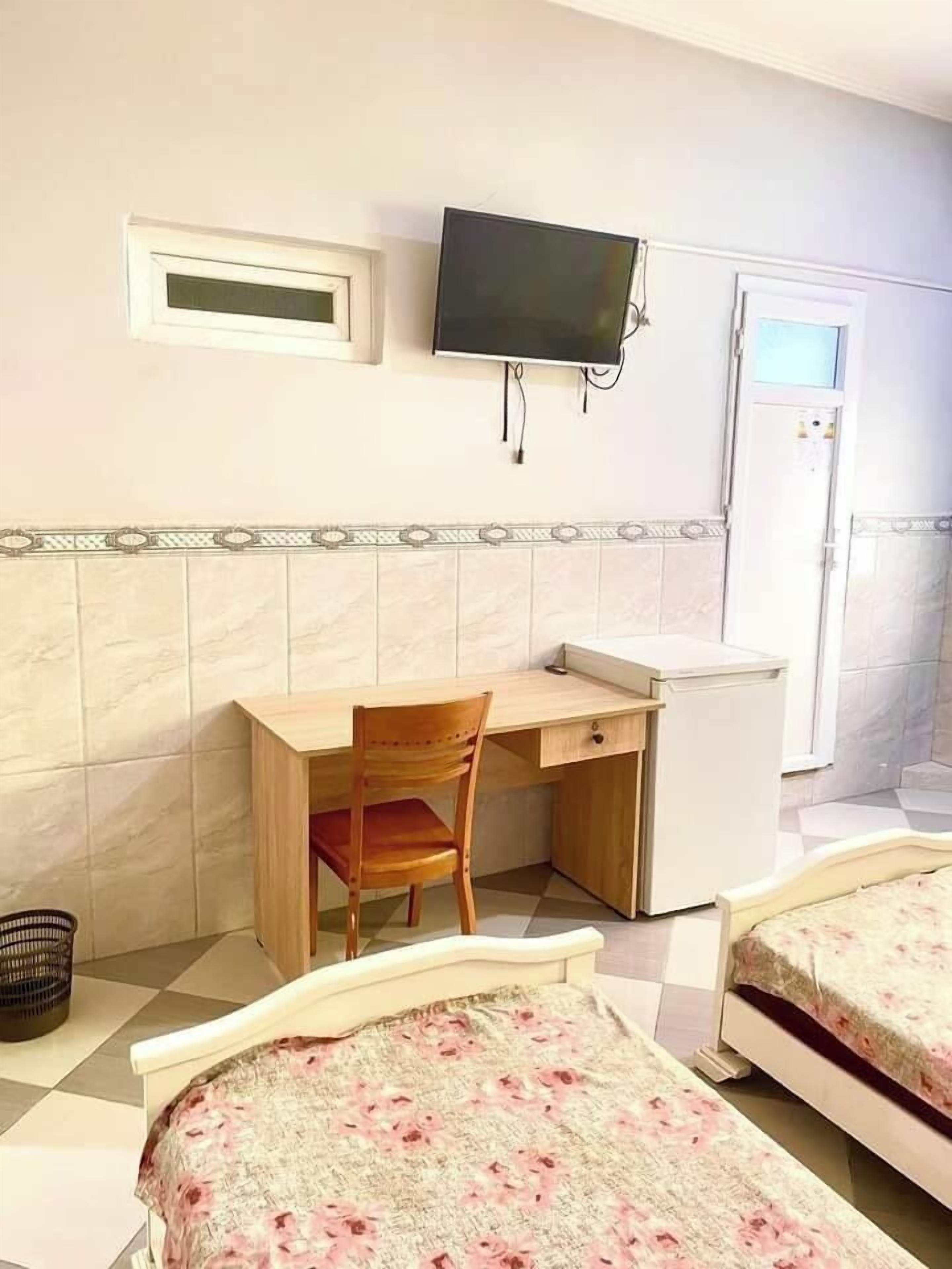 A bedroom with a bed, a desk, a chair, a television, and a refrigerator.