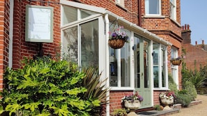 A corner house with a signboard, a glass door, and a gravel driveway. - The Corner House (Lowestoft)
