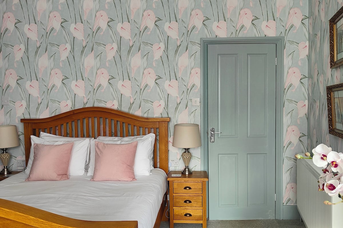A bedroom with a wooden bed, two bedside tables with lamps, a dresser, and a door.