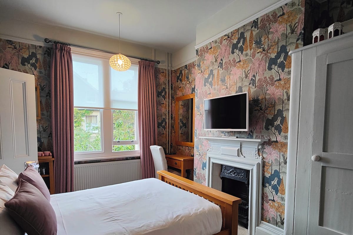 A bedroom with a bed, a television, a fireplace, and a window with curtains.