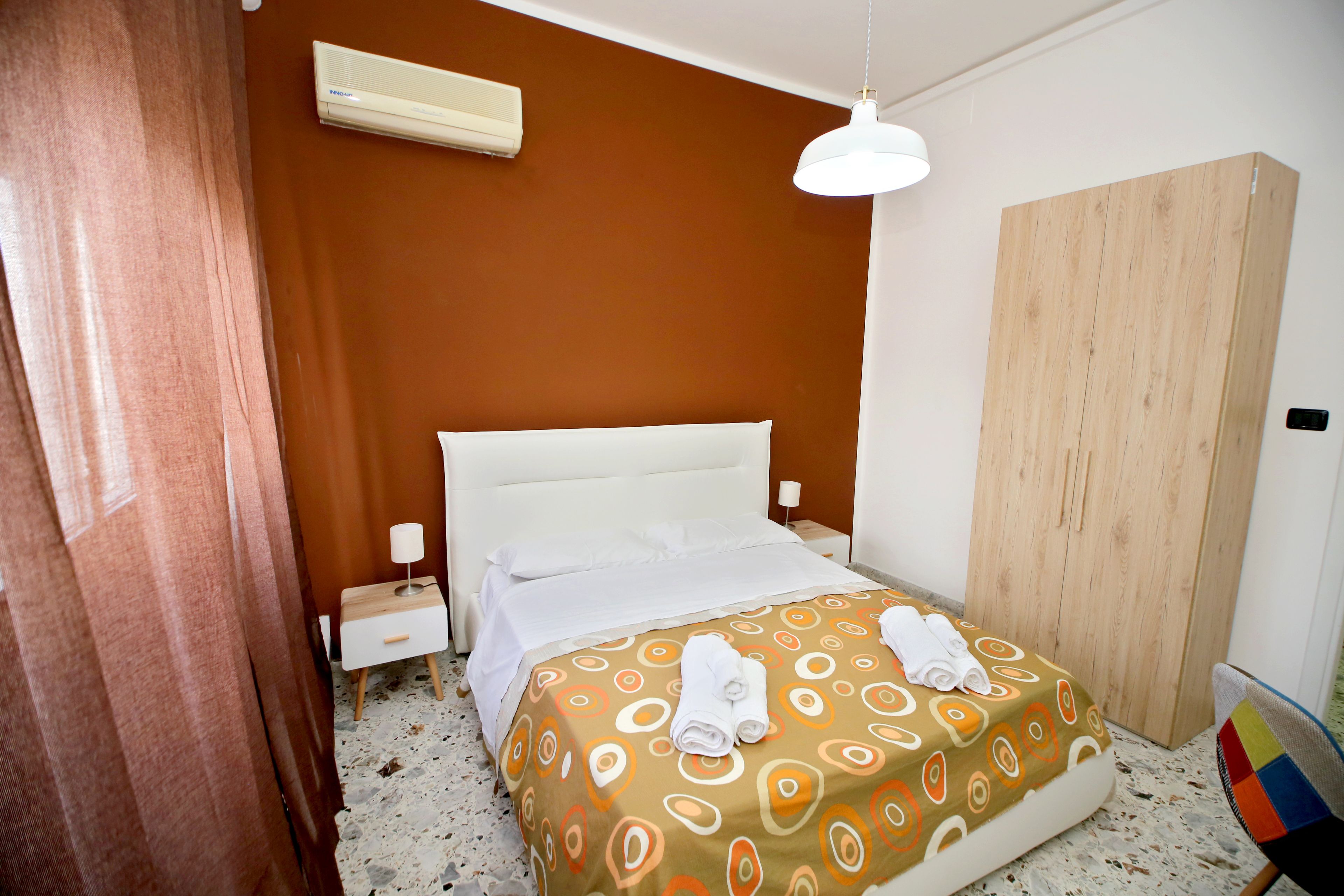 Quarto de hotel com cama, guarda-roupa de madeira, mesa de cabeceira e ar condicionado.