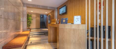 A reception area with a wooden desk, a computer, and a television on the wall.