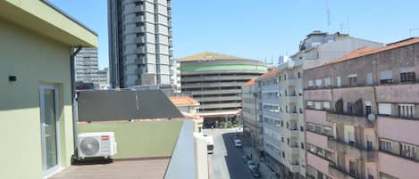 A high-rise building with a modern design, a rooftop terrace with a wooden deck, and a street view with parked cars and a bus.