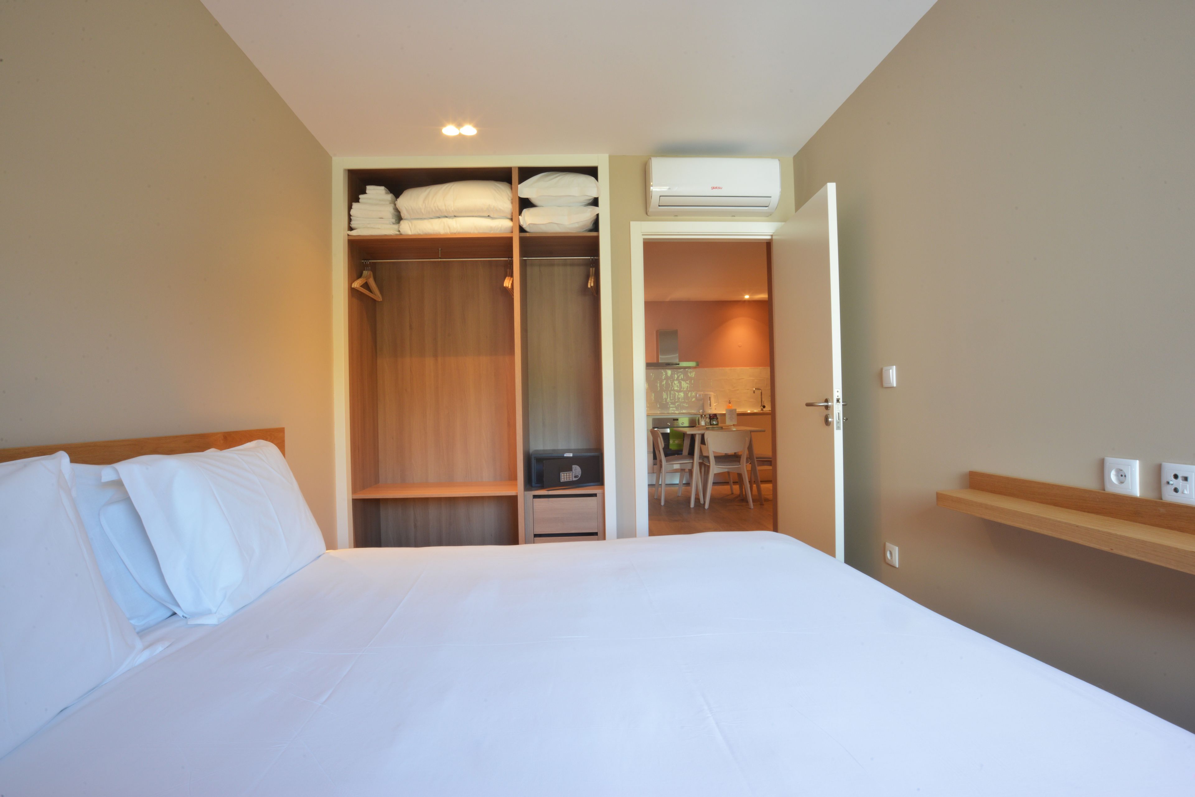 Quarto de hotel com uma cama, um guarda-roupa, uma escrivaninha com cadeira e um aparelho de ar condicionado.