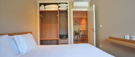 A hotel room with a bed, a wardrobe, a desk with a chair, and an air conditioning unit.