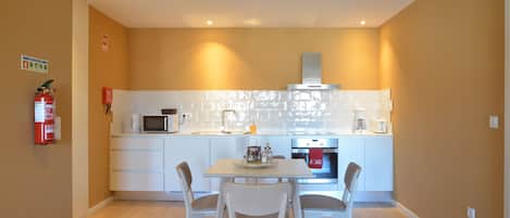 A compact kitchen with white cabinets, a microwave, a stove, and a dining table with chairs.