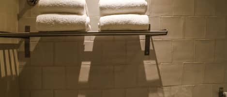 A bathroom with two white towels stacked on a metal towel rack against a tiled wall.