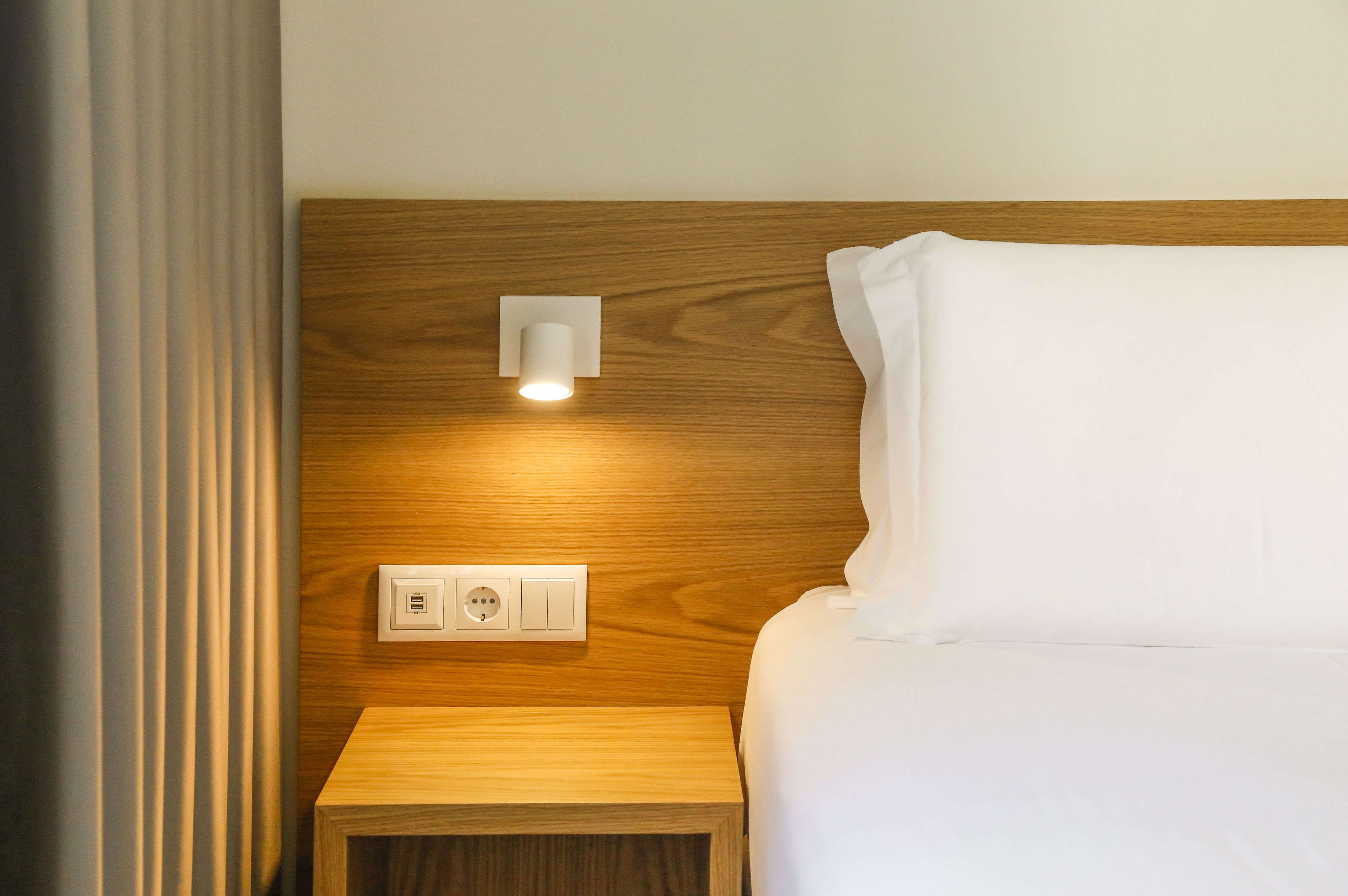 A neatly made bed with a wooden headboard, a bedside table, and a wall-mounted light fixture.
