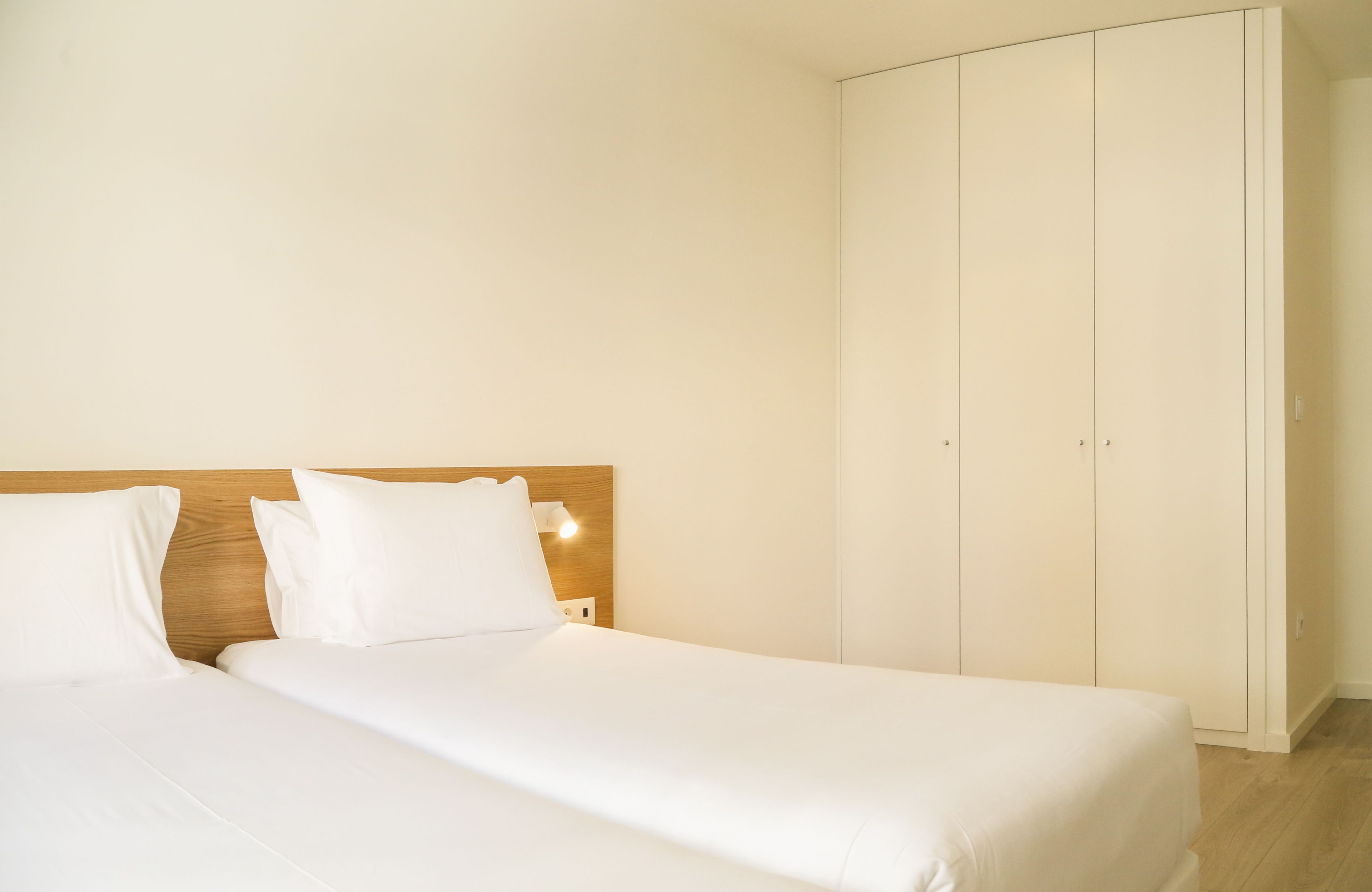 A bedroom with two beds, a wooden headboard, and a wardrobe.