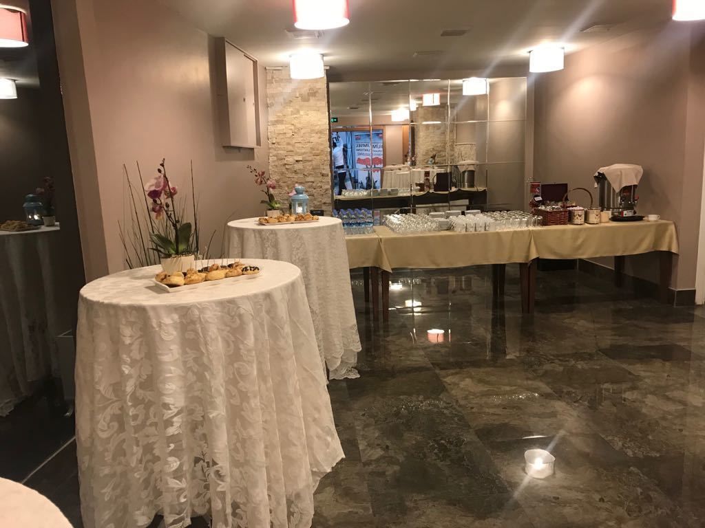 A hotel lobby with two round tables covered with white tablecloths, a long table with glassware, and a coffee station.