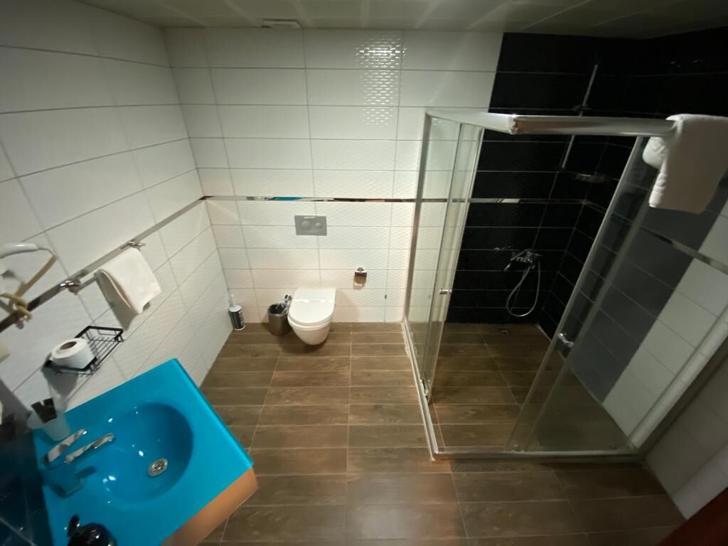 Un baño con un lavamanos azul, un inodoro y una zona de ducha con mampara de cristal.
