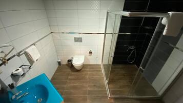 Un baño con un lavamanos azul, un inodoro y una zona de ducha con mampara de cristal.
