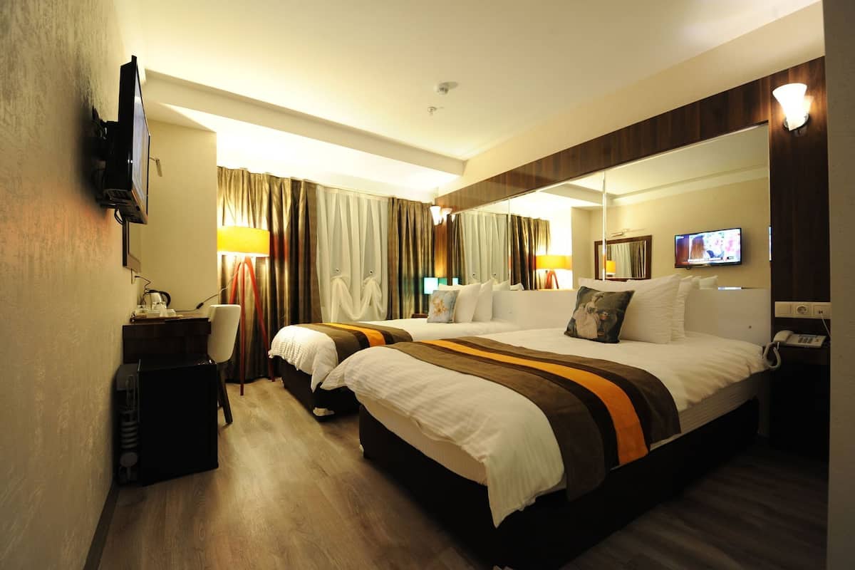 A hotel room with a large bed, a desk with a lamp, a television, and a mirror.