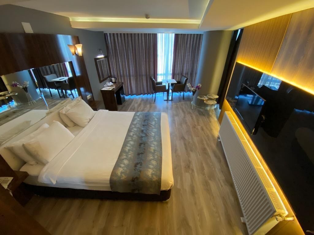 A hotel room with a large bed, a desk, a chair, and a small table with a vase of flowers.