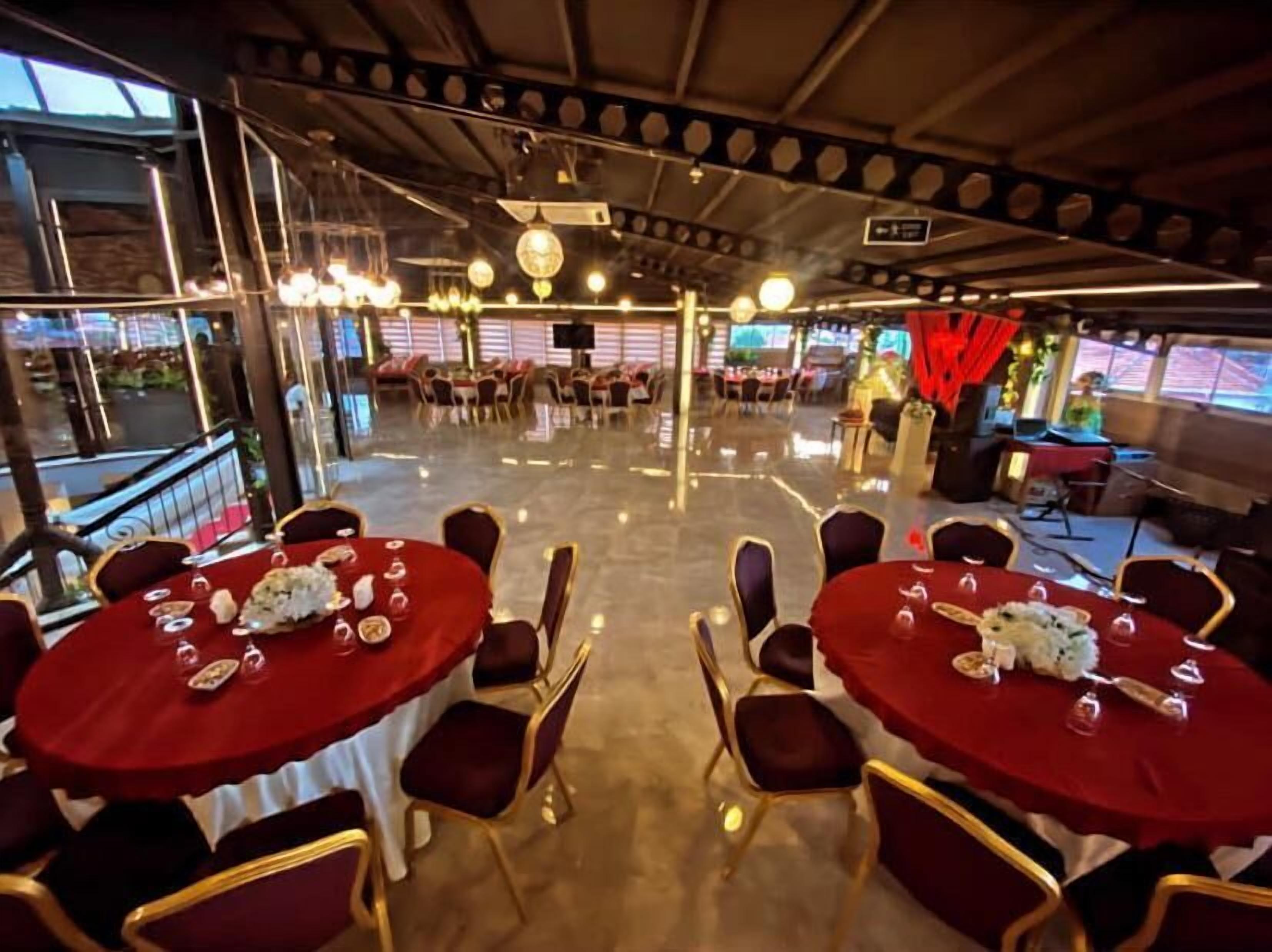 Ein Restaurant mit runden Tischen, roten Tischdecken, goldenen Stühlen und einem polierten Boden.