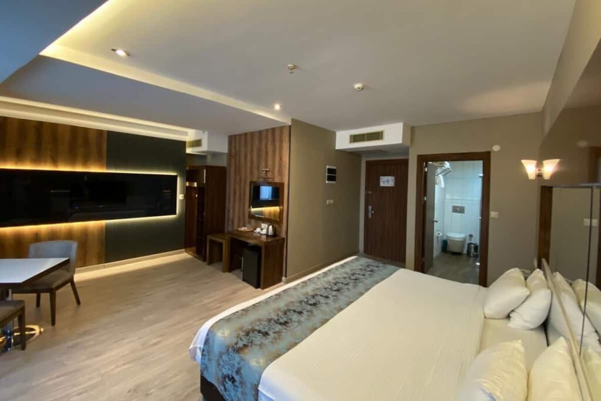 A modern hotel room with a large bed, a desk, a TV, and a balcony.