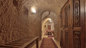A stone-walled hallway with a wooden bench and a patterned carpet, leading to a room with a bed and a mirror. - Yoruk Stone House (Avanos)