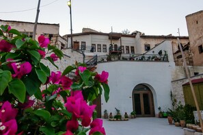 A courtyard with a white building, a wooden door, and potted plants. - Yoruk Stone House (Avanos)