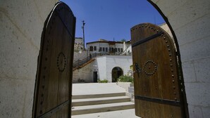 A set of wooden double doors leading to a building with a white facade and a staircase. - Yoruk Stone House (Avanos)