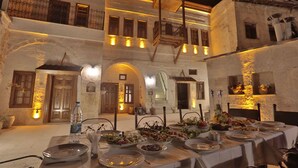 An outdoor dining area with a table set for a meal, surrounded by stone buildings with arched doorways and balconies. - Yoruk Stone House (Avanos)