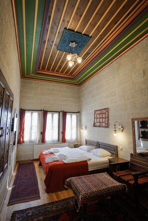 A bedroom with a wooden ceiling, two beds, a window with curtains, a bedside table, and a nightstand. - Yoruk Stone House (Avanos)