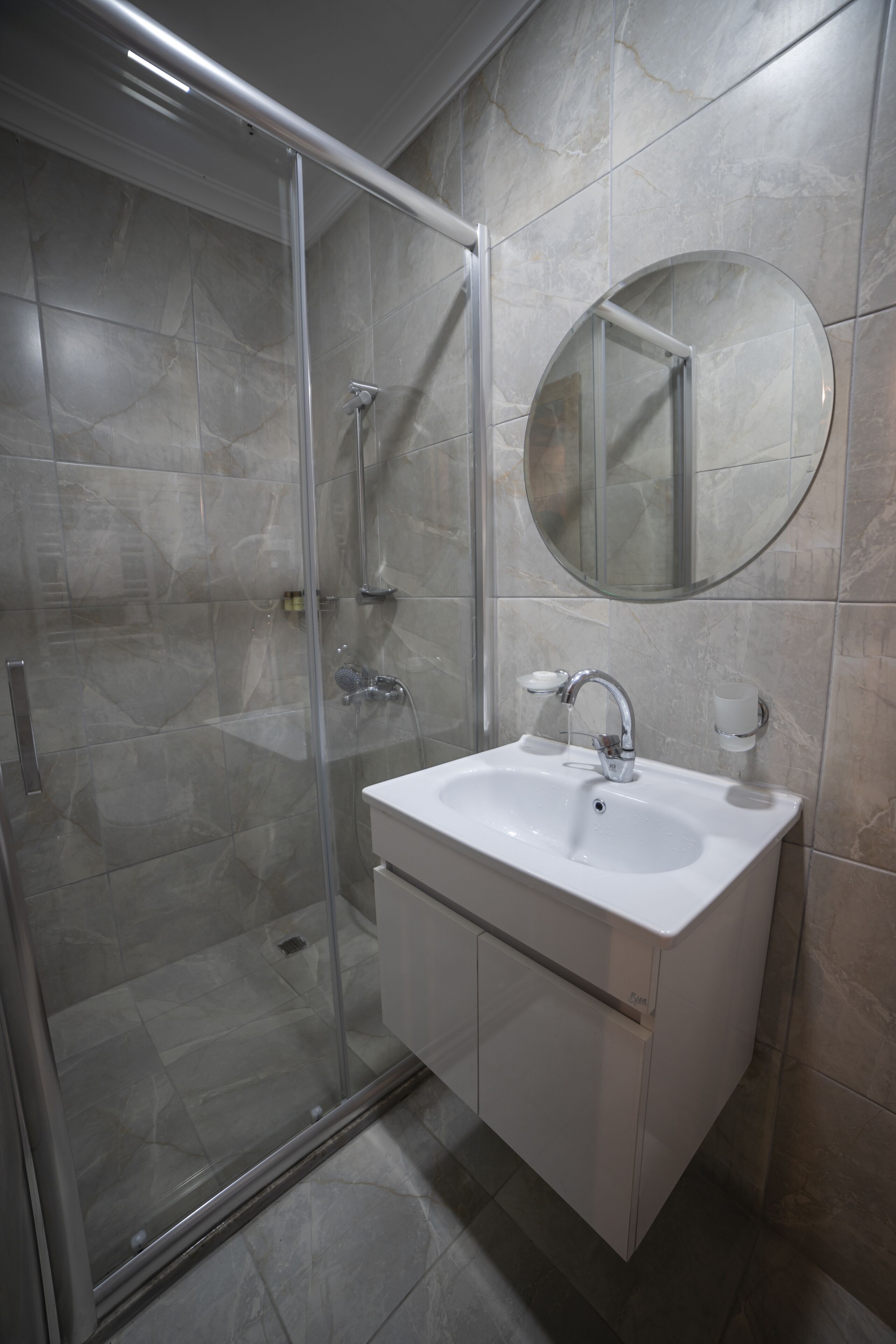 A modern bathroom with a glass-enclosed shower, a white sink with a mirror above it, and tiled walls.
