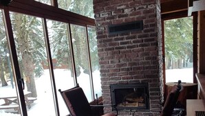 Un espacio exterior acogedor con chimenea de ladrillo, ventanas amplias y mobiliario de madera.