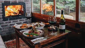 Un comedor acogedor con chimenea de ladrillo, una mesa dispuesta con platos de comida, copas de vino y una botella de vino.