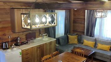 Interior acogedor de una cabaña con una mesa de comedor de madera, sillas, una kitchenette y un sofá con cojines amarillos.