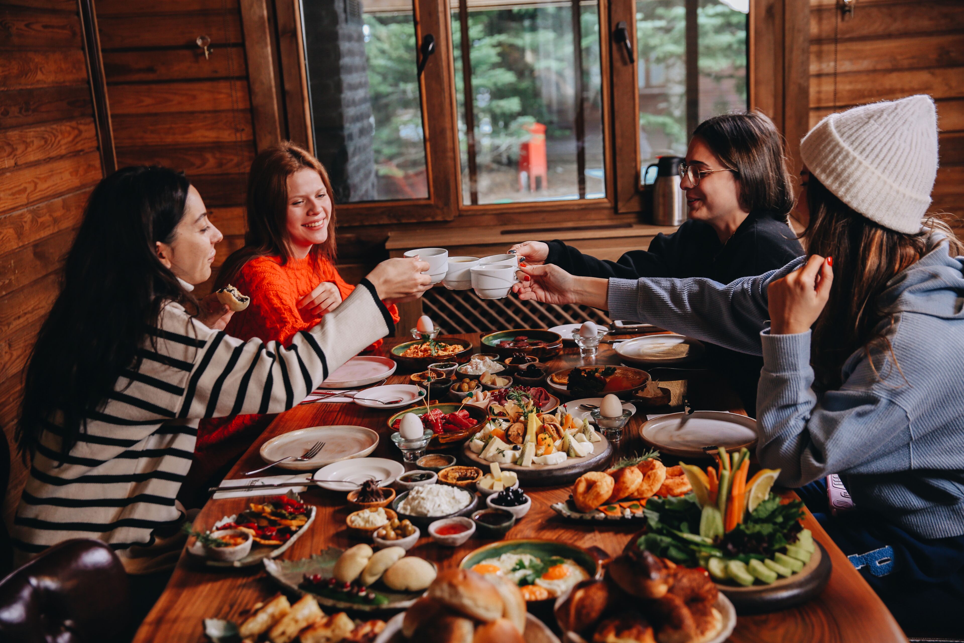 Un groupe de personnes est réuni autour d’une table à manger en bois, où sont disposés différents plats, ce qui laisse supposer qu’il s’agit d’un repas partagé.