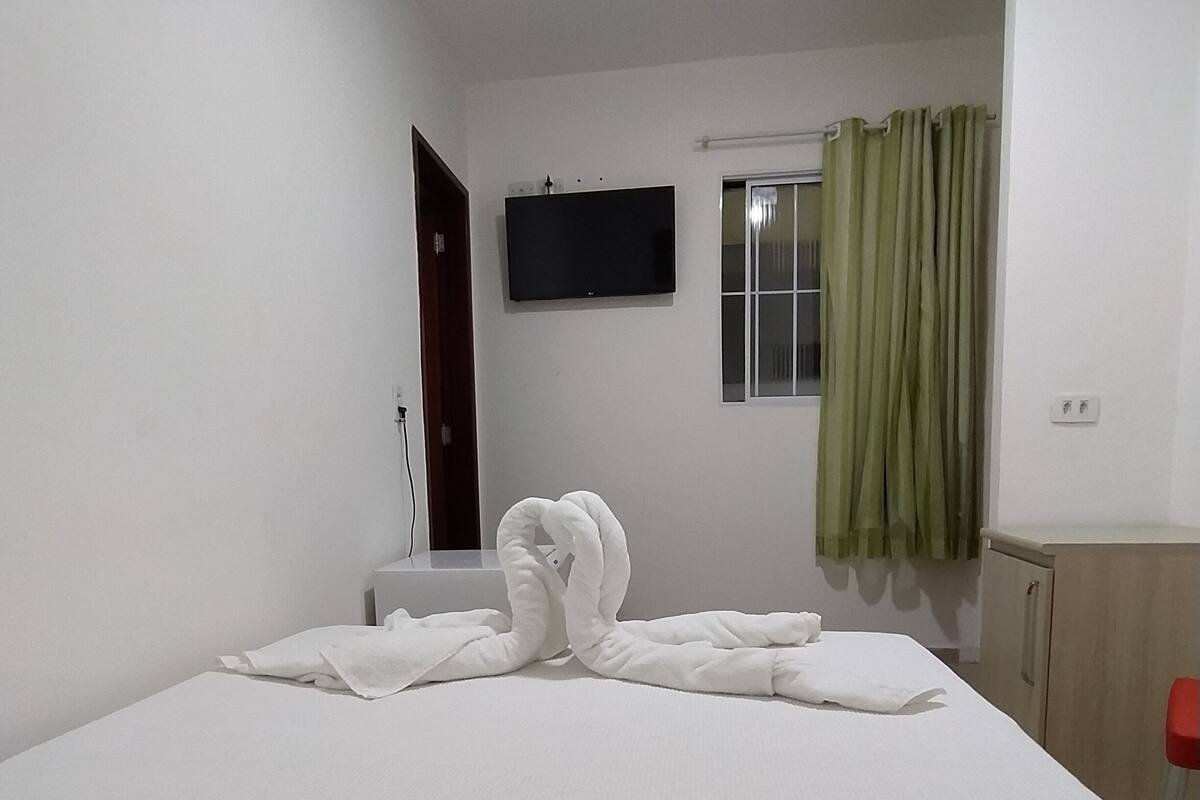 Habitación de hotel con cama, televisor de pantalla plana en la pared, ventana con cortinas y un armario de madera.
