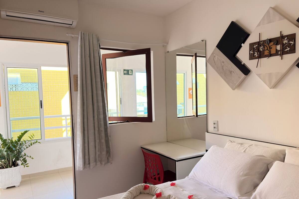 Un dormitorio con cama, escritorio, silla, planta en maceta y ventana con cortinas.