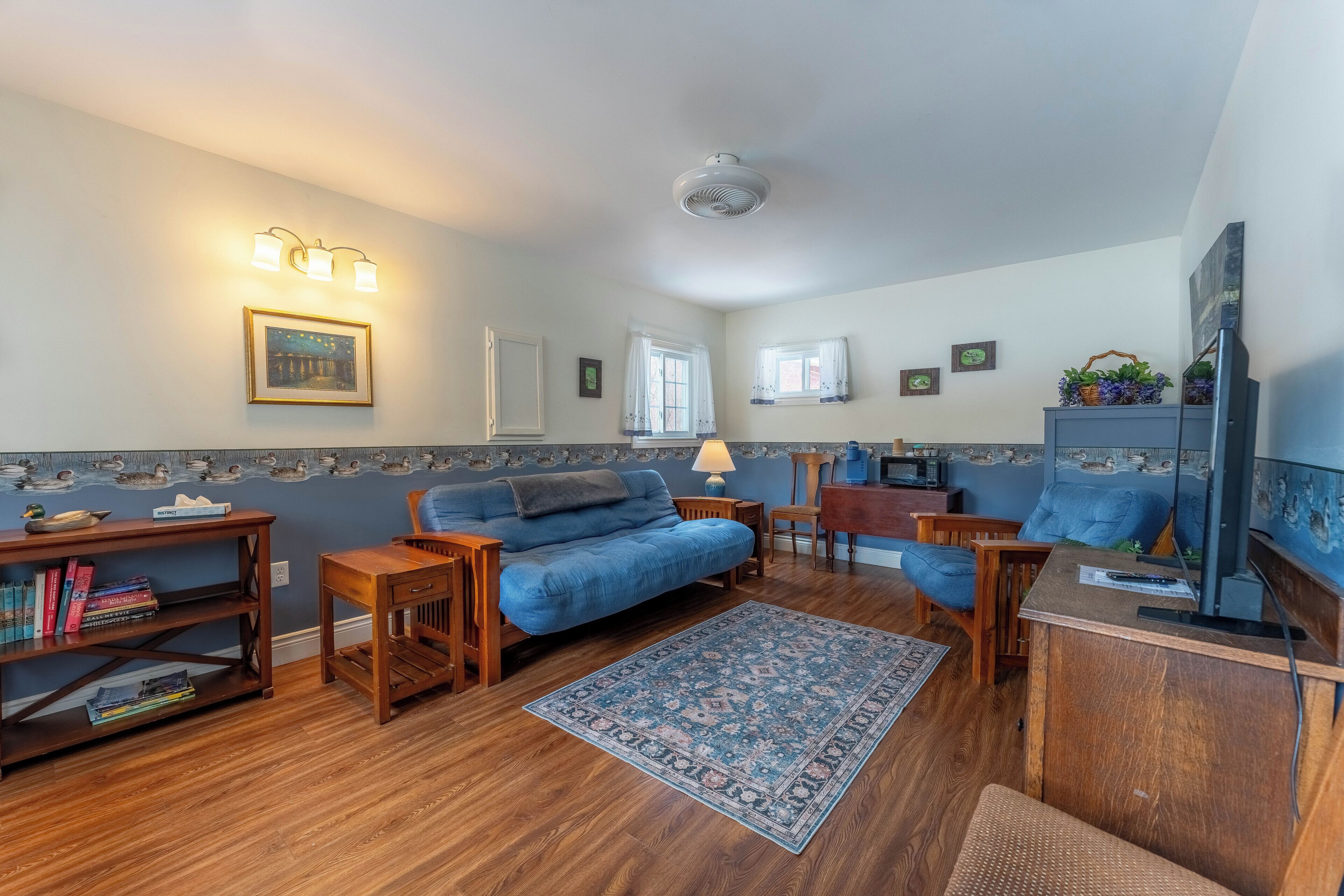 Uma sala de estar aconchegante com um sofá azul, mesinhas de madeira, um tapete estampado e uma televisão.