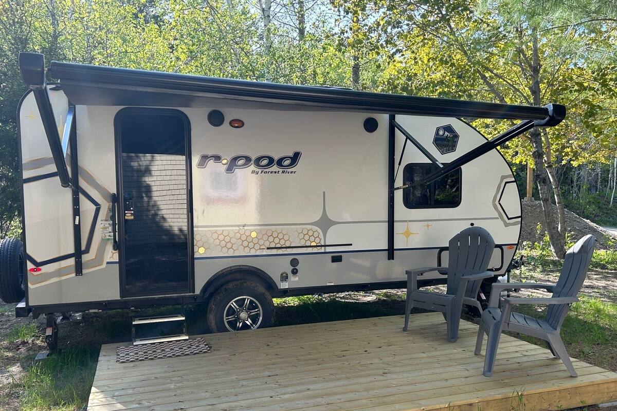 Una caravana recreativa con el logotipo 'r.pod', una pequeña terraza y dos sillas.