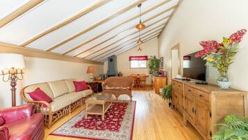 Un salon spacieux avec un plafond haut, un plancher en bois, un canapé, une table basse et un téléviseur.