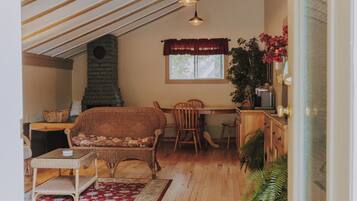 A cozy loft-style room with a sloped ceiling, wooden floors, a fireplace, wicker furniture, and hanging pendant lights.