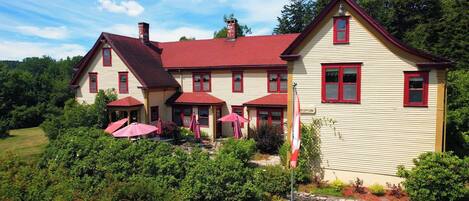 A two-story building with a red roof and beige siding, featuring a reception area with outdoor seating and umbrellas.